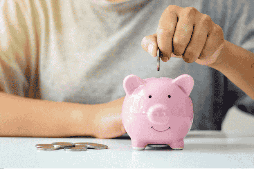 Main insérant une pièce de monnaie dans une tirelire rose, symbole d’épargne