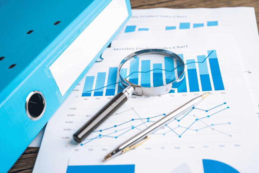 Loupe posée sur des graphiques financiers imprimés, illustrant l’analyse de données bancaires mensuelles.